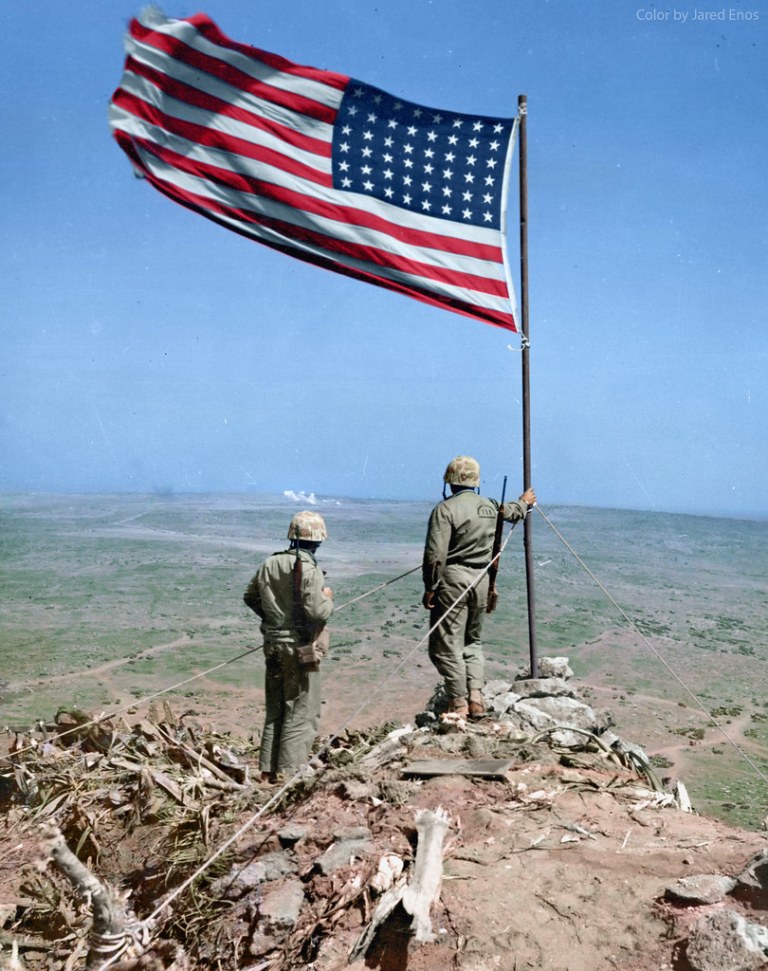 Two U.S. Marines of the 4th Marine Division stand atop Mt. Suribachi, overlooking the remainder of Iwo Jima, part of which is still held by the Japanese. ca. Feb-Mar 1945.jpg