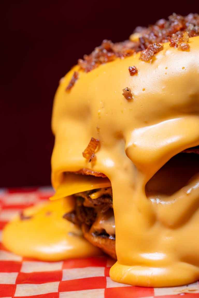 A delicious close-up shot of a burger overflowing with melted cheese on a checkered surface..jpg
