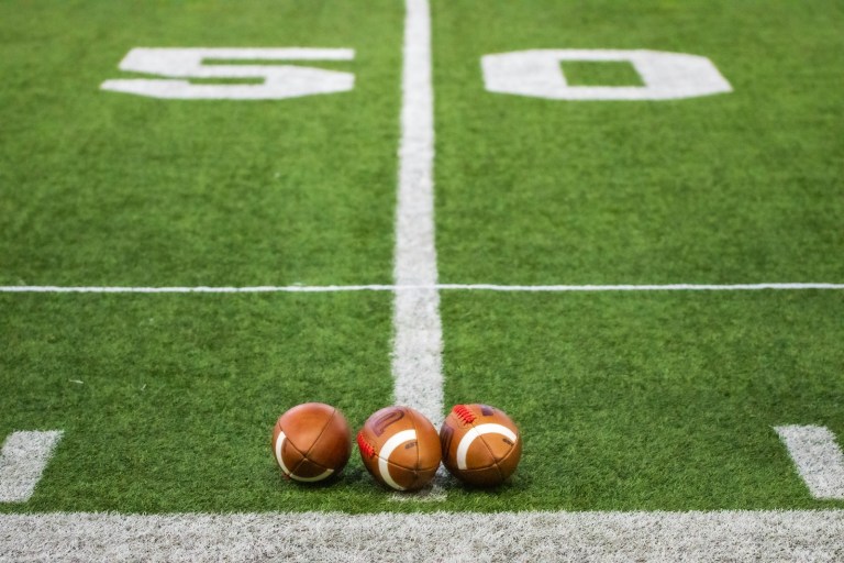 Three footballs sitting on a football field.jpg